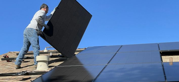 A worker installs solar panels on a sunny day, highlighting renewable energy solutions.